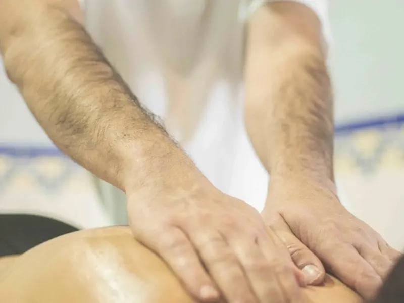 Las manos de un fisioterapeuta trabajan sobre la espalda de un paciente.